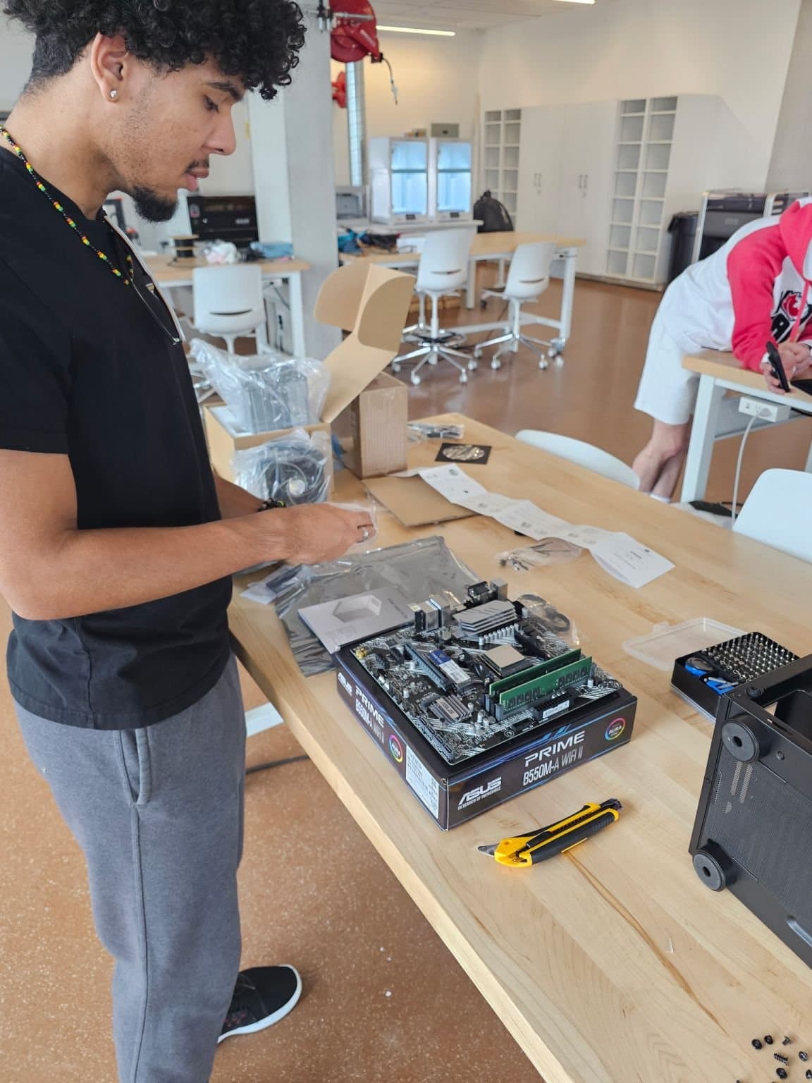 Kalan Roye assembling an ASUS PRIME B550M-A motherboard at a wooden workbench in the Morrissette Maker Space